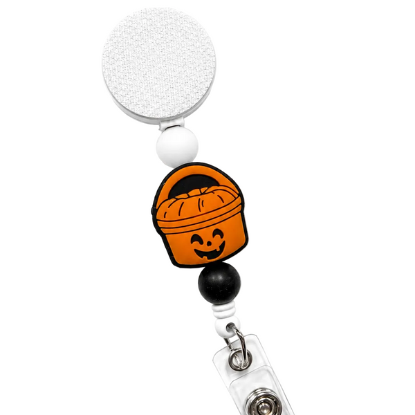 Glow in the dark pumpkin bucket badge reel featuring an orange Halloween trick-or-treat bucket with black and white decorative beads, retractable badge reel, and secure badge holder attachment.