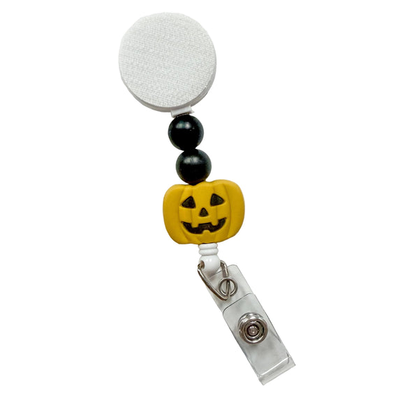 Golden Yellow Jack-o'-Lantern badge reel featuring a smiling carved pumpkin with black decorative beads, retractable badge reel functionality, and a secure badge holder attachment.