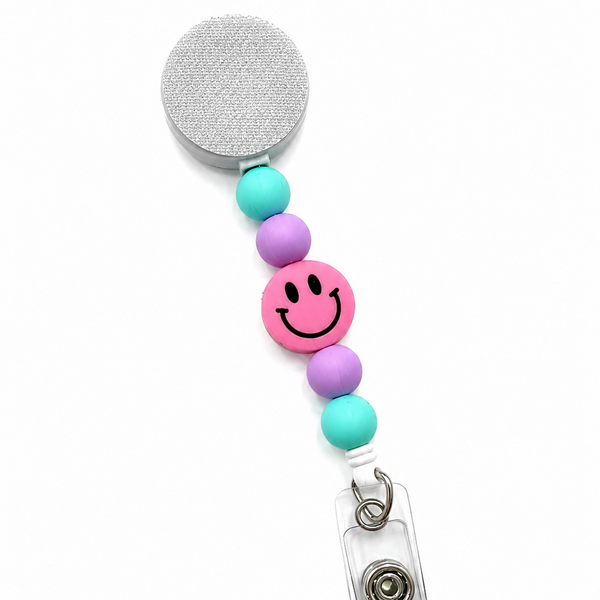 Pink Smiley Face badge reel featuring a pink happy face design with pastel mint and lavender decorative beads, retractable badge reel functionality, and secure badge holder attachment.